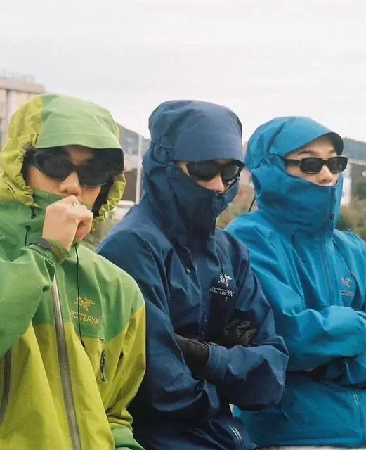 Three people in Arc'teryx shells braced against the weather.